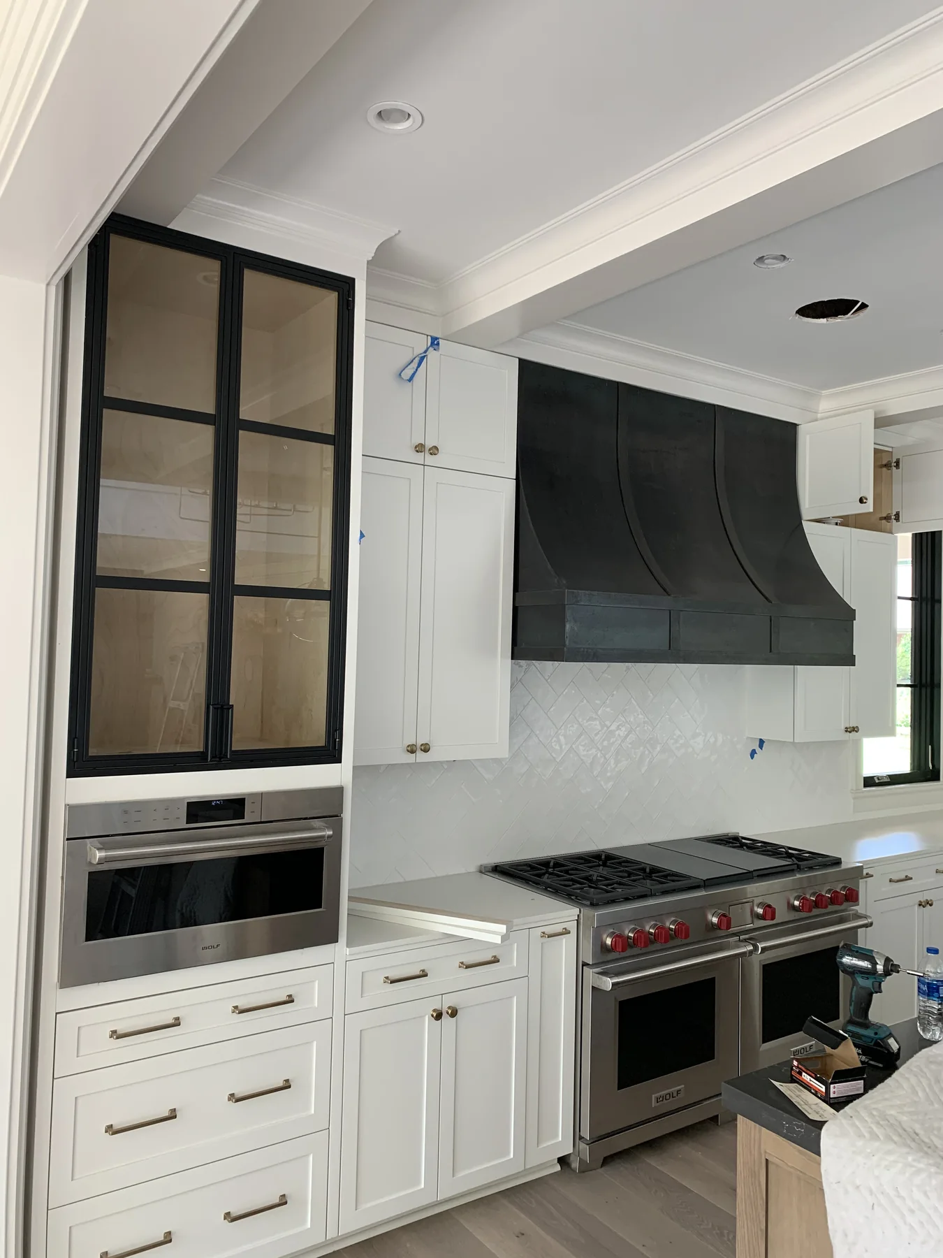 Tall black custom metal range hood installed in a bright residential kitchen